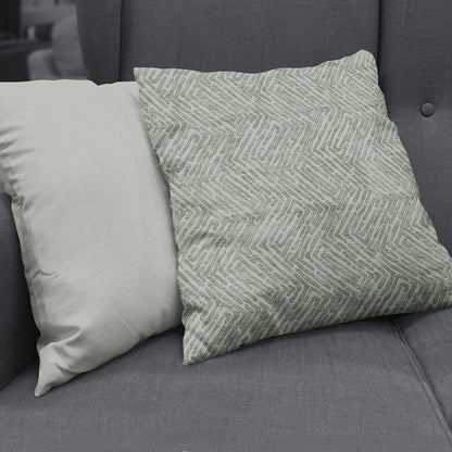 Two square throw pillows on a dark gray sofa, made with vapor velvet geometric fabric: left solid pale beige, right sage green with a chevron geometric pattern.
