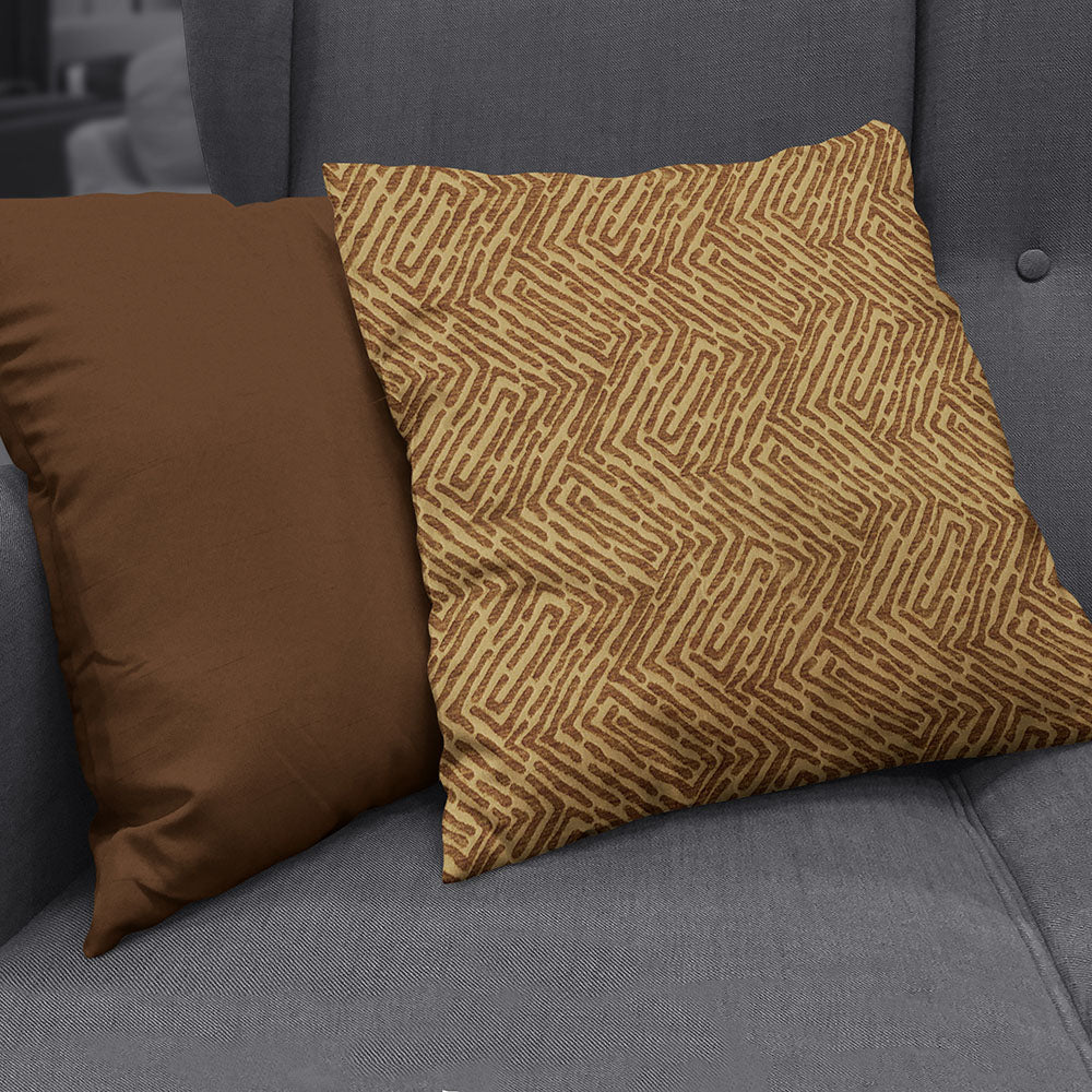 Two square throw pillows on a gray sofa: a solid brown pillow on the left and a tan pillow with a brown geometric pattern.