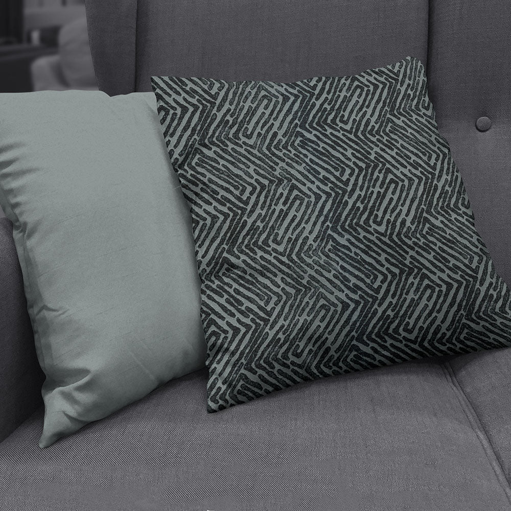 Grey sofa with two cushions: left solid dusty sage green, right dark teal with a geometric maze pattern.