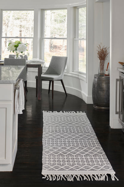 Light gray geometric lattice rug with fringe, on dark hardwood floor in a bright modern farmhouse dining area.