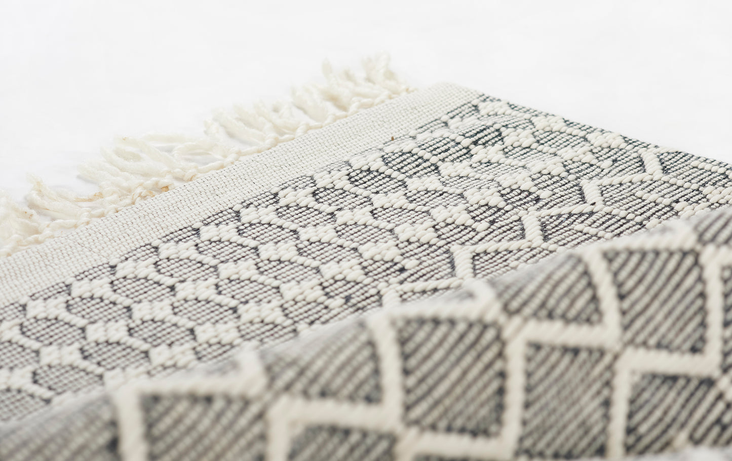 Close-up of a black and cream woven throw with geometric diamond patterns and fringe.