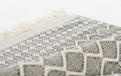 Close-up of a black and cream woven throw with geometric diamond patterns and fringe.