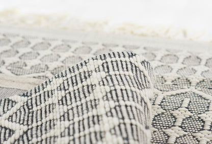 Close-up of a black-and-white woven rug with geometric diamond motifs; folded edge curling up.