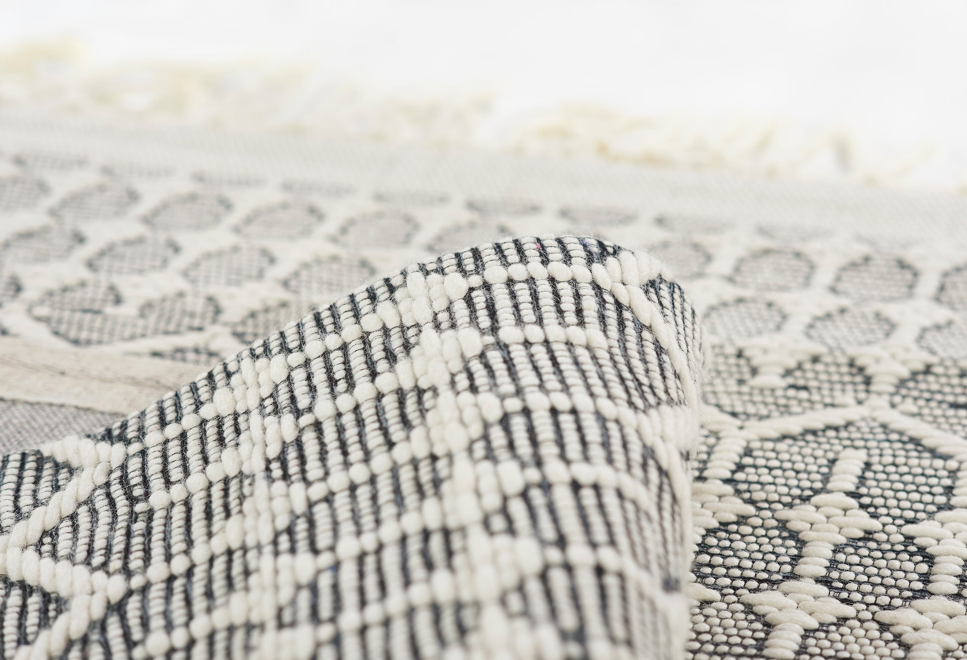 Close-up of a black-and-white geometric woven rug, folded corner showing intricate pattern and texture.