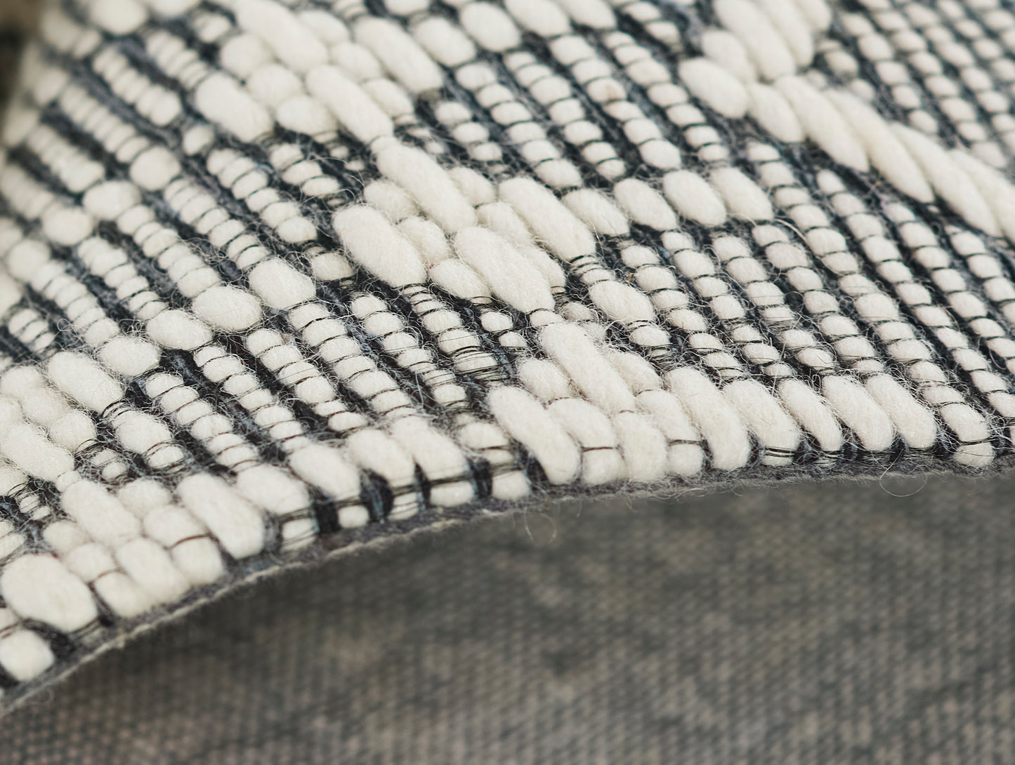 Close-up of a black & cream woven rug with chunky looped yarns & geometric pattern, edge visible.