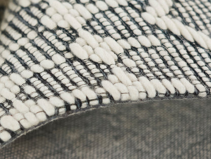 Close-up of a black & cream woven rug with chunky looped yarns & geometric pattern, edge visible.