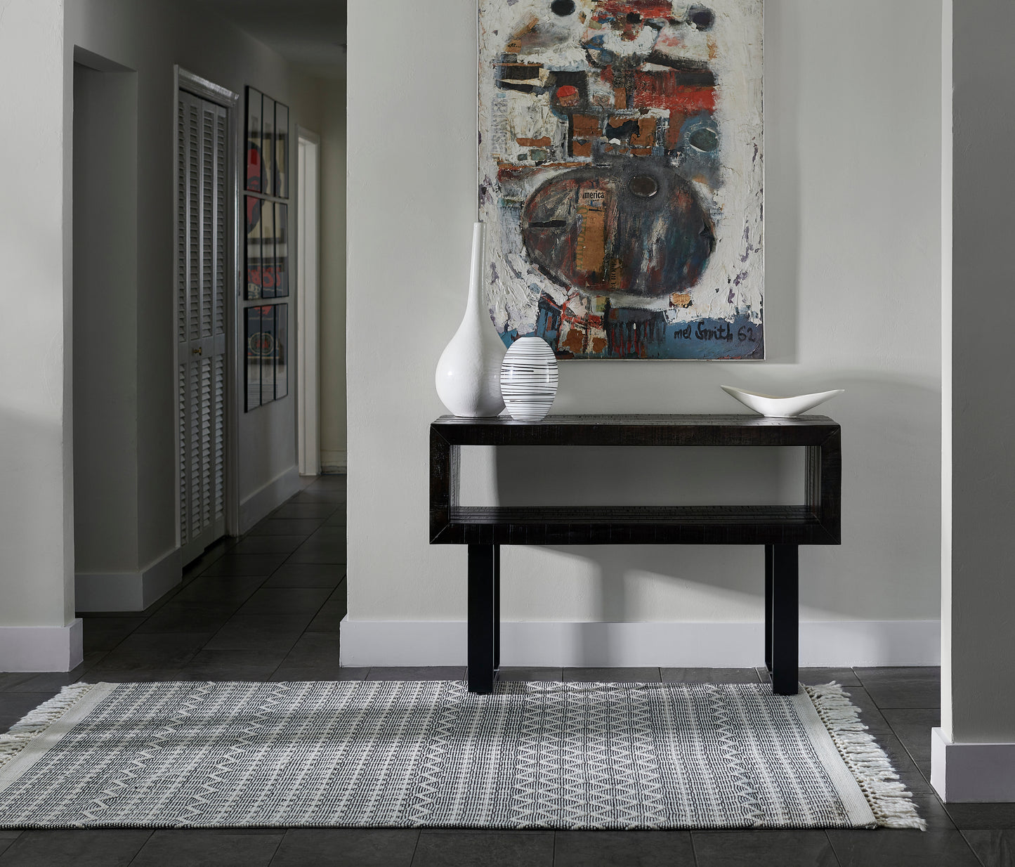 Black wooden console table with open lower shelf, white vases and a bowl on top, gray walls with abstract art.
