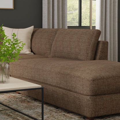 Taupe solid fabric sofa with chaise in a modern living room, beige pillow, glass-top coffee table, and a plant.