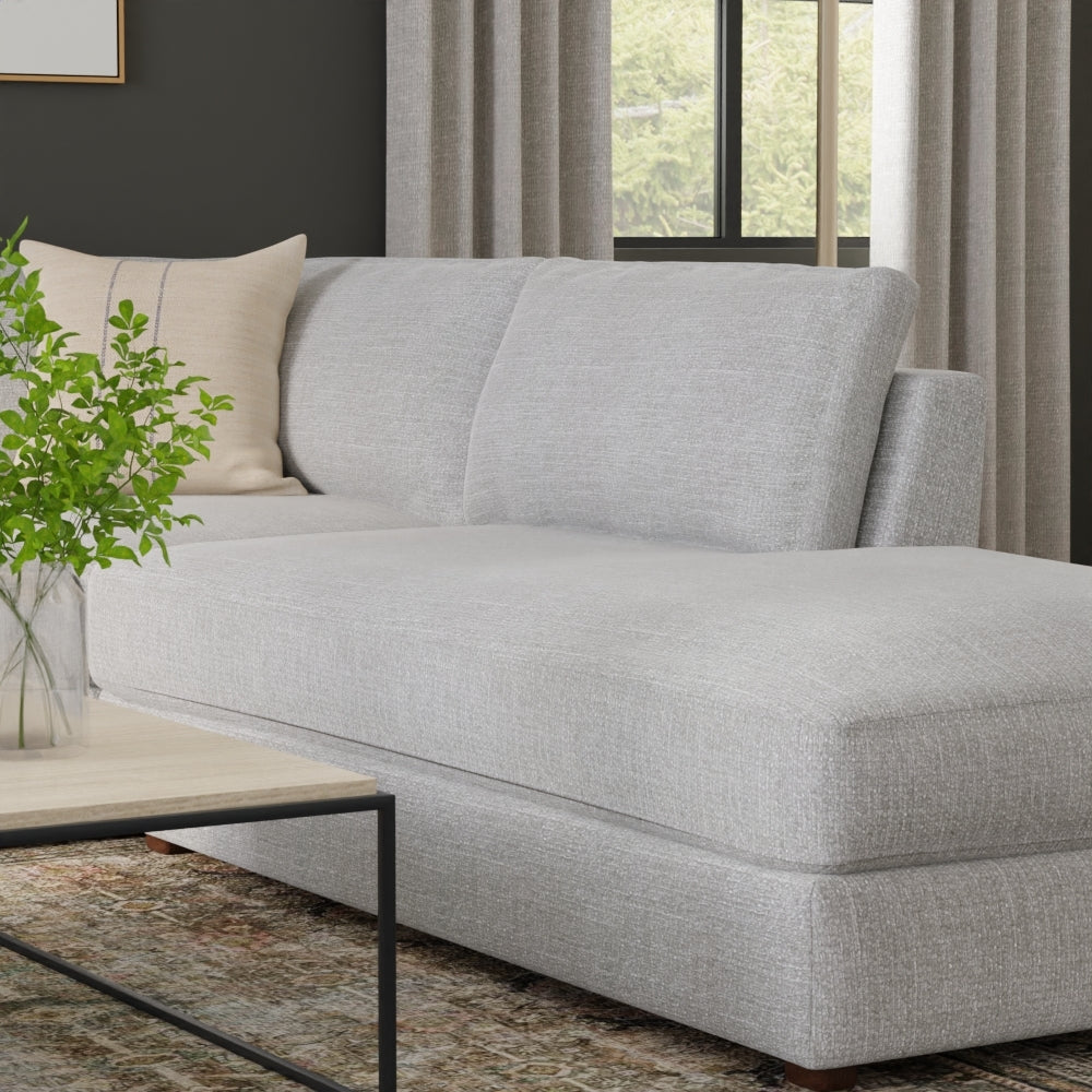 Light gray fabric sectional sofa with chaise, beige throw pillow, modern living room with wood coffee table and greenery.