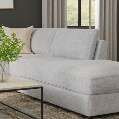 Light gray fabric sectional sofa with chaise, beige throw pillow, modern living room with wood coffee table and greenery.
