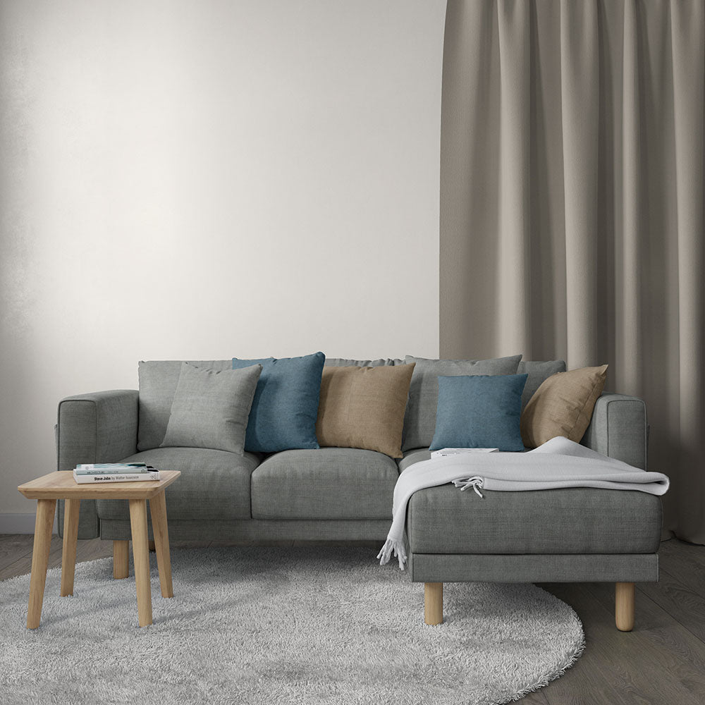 Grey solid fabric upholstery in a living room scene; visible is a gray sectional sofa with blue and tan cushions, light wood legs, a white throw blanket, and a round wooden side table on a gray rug.