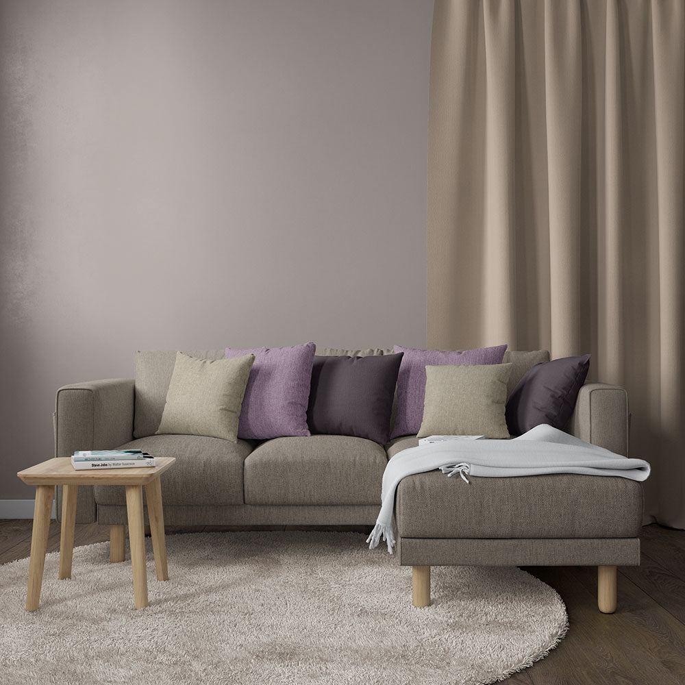 Beige solid upholstery fabric used on a sofa & chaise in a living room setup; purple & beige cushions, light wood side table, gray throw, circular cream rug, and beige curtains.
