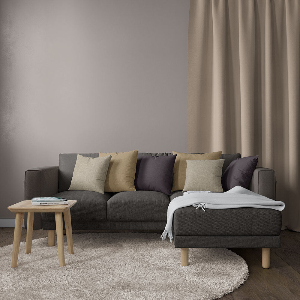 Charcoal gray sectional sofa with light wood legs, mixed cushions, cream throw, round beige rug, wooden side table.