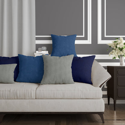 Beige fabric sofa with blue & gray cushions in a chic living room; dark wood side table, white framed wall panels, vase of flowers.