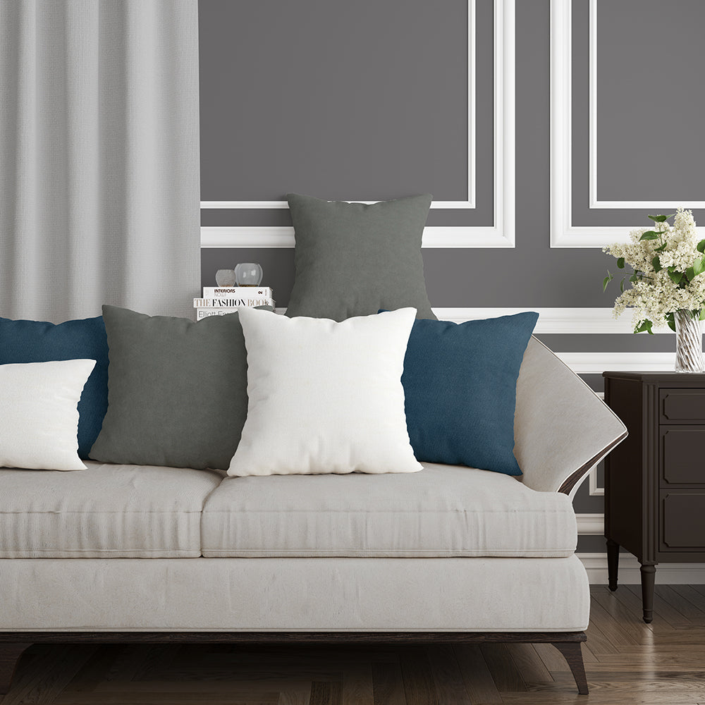 Beige sofa upholstered in Benjamin Snow solid fabric, with white, gray, and teal throw pillows, dark wood side table, gray paneled walls, and a vase of white flowers.