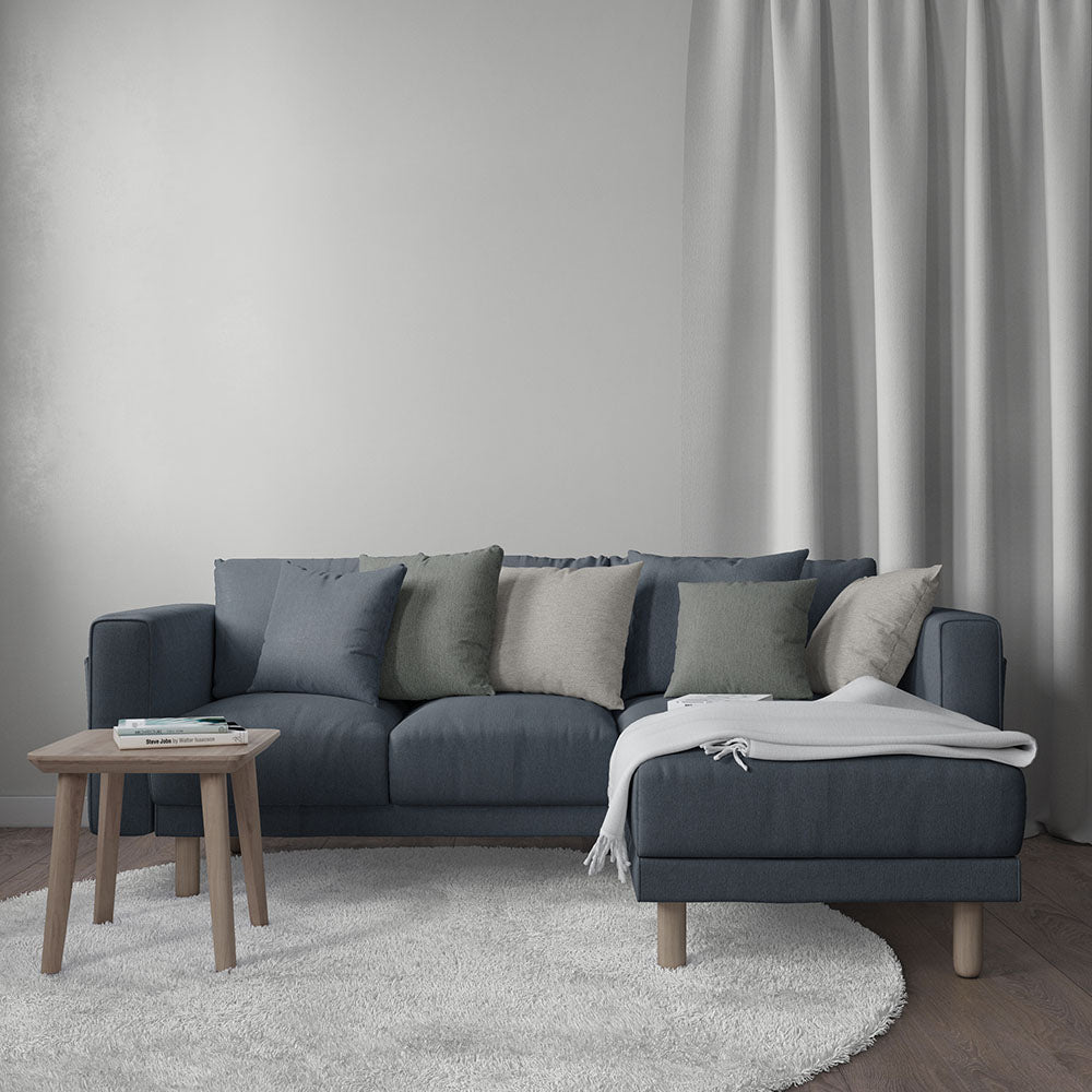 L-shaped navy sofa with mixed cushions, white throw, wooden legs, round side table, beige rug.