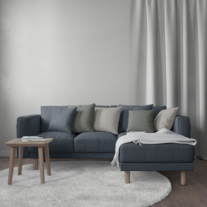 L-shaped navy sofa with mixed cushions, white throw, wooden legs, round side table, beige rug.