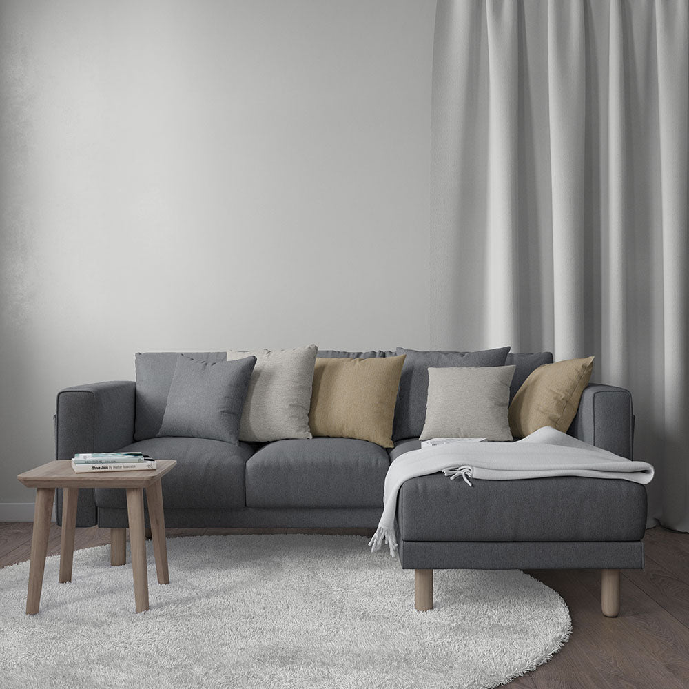 Dark gray L-shaped sectional sofa with neutral cushions, white throw, round wood side table, light rug and curtains.