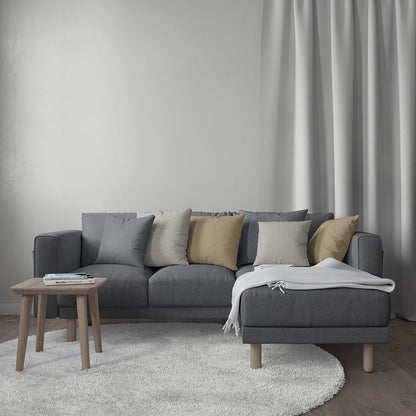 Dark gray L-shaped sectional sofa with neutral cushions, white throw, round wood side table, light rug and curtains.
