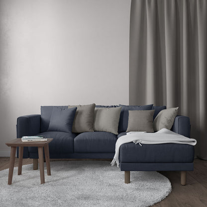 Dark blue sectional sofa with chaise, blue and beige cushions, wooden legs, beige throw, small wooden coffee table.