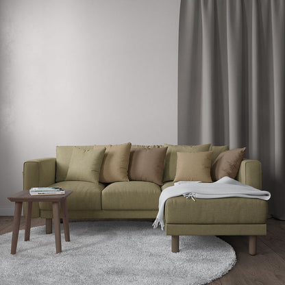 Sectional sofa upholstered in wheat solid textured fabric; beige cushions and a white throw, chaise on the right, and a wooden side table on a gray rug.