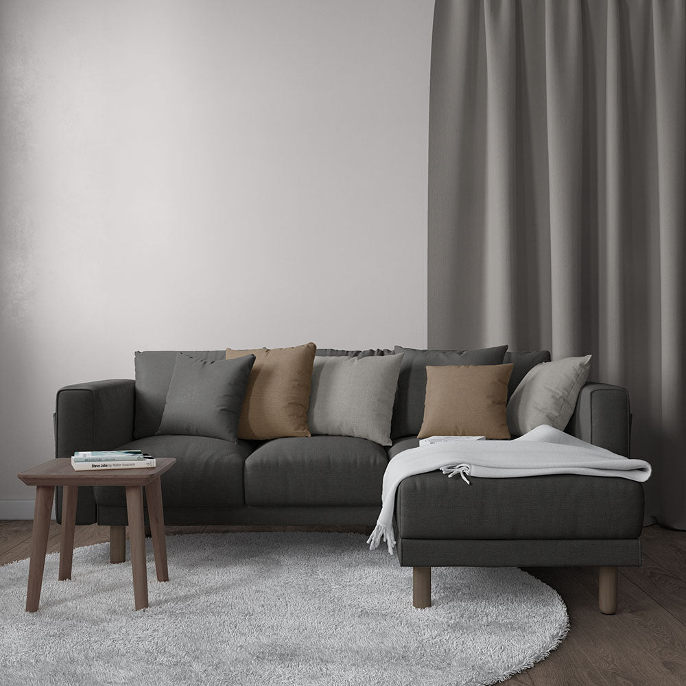 Dark gray sectional sofa with beige and gray cushions, white throw on the ottoman, wooden coffee table, gray curtains.