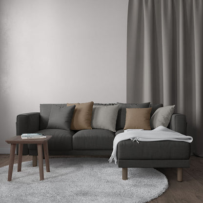 Dark gray sectional sofa with beige and gray cushions, white throw on the ottoman, wooden coffee table, gray curtains.