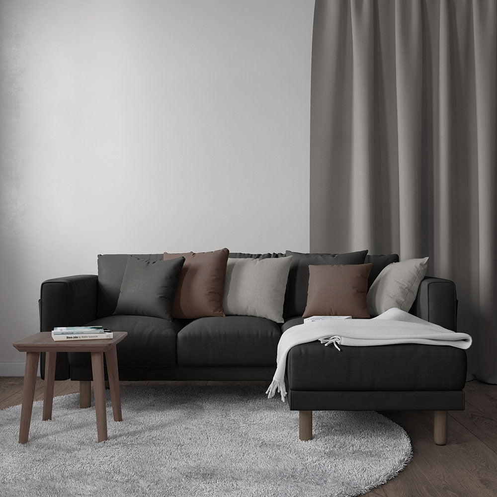 Charcoal sectional upholstered in solid textured fabric; cushions in gray and brown, chaise with a light gray throw; round wood coffee table on a soft gray rug.