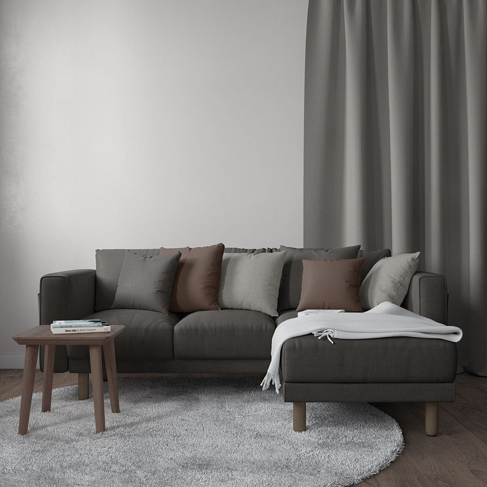 Charcoal gray sectional with chaise, brown and gray cushions, wood legs, gray rug, wooden side table, white throw blanket.