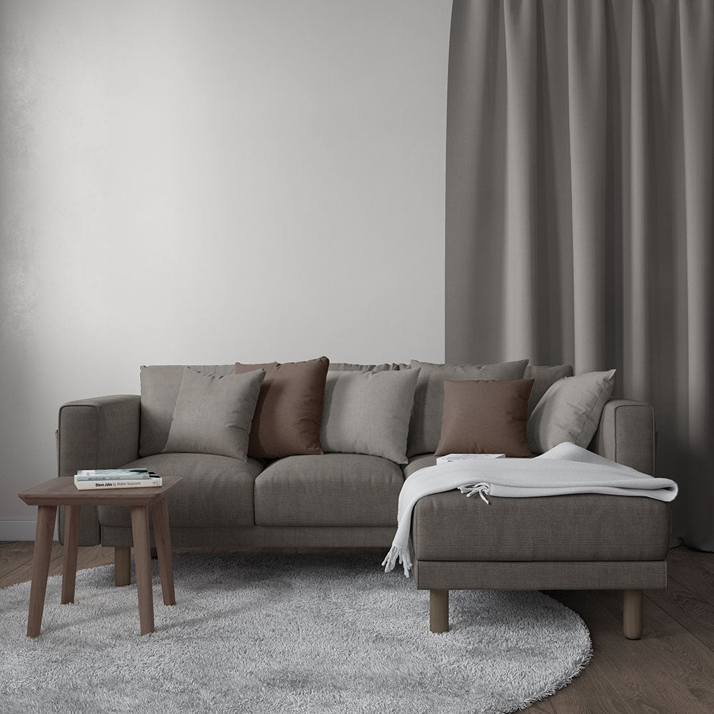 Gray sectional sofa with brown and gray cushions, chaise, wooden legs; light throw, round rug, small wooden side table.