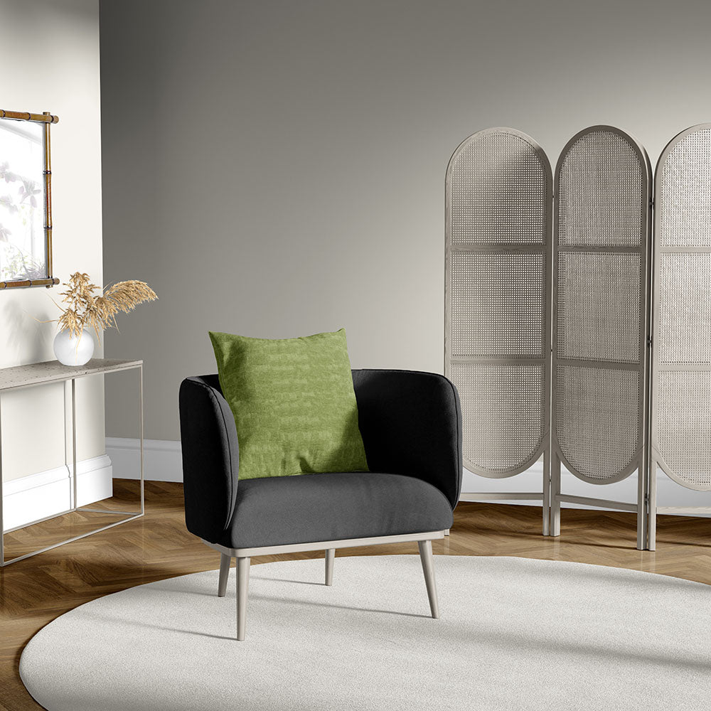 Modern charcoal armchair with light wood legs and a green cushion in a neutral living room with a wicker three-panel room divider.