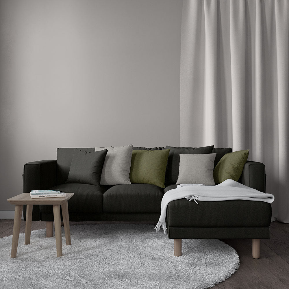 Dark gray sectional sofa with olive green and gray cushions, white throw, round wood coffee table, light rug.