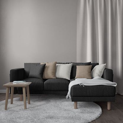 Sectional sofa upholstered in charcoal solid fabric with beige, taupe and white cushions, light gray throw, wooden coffee table and soft curtains.