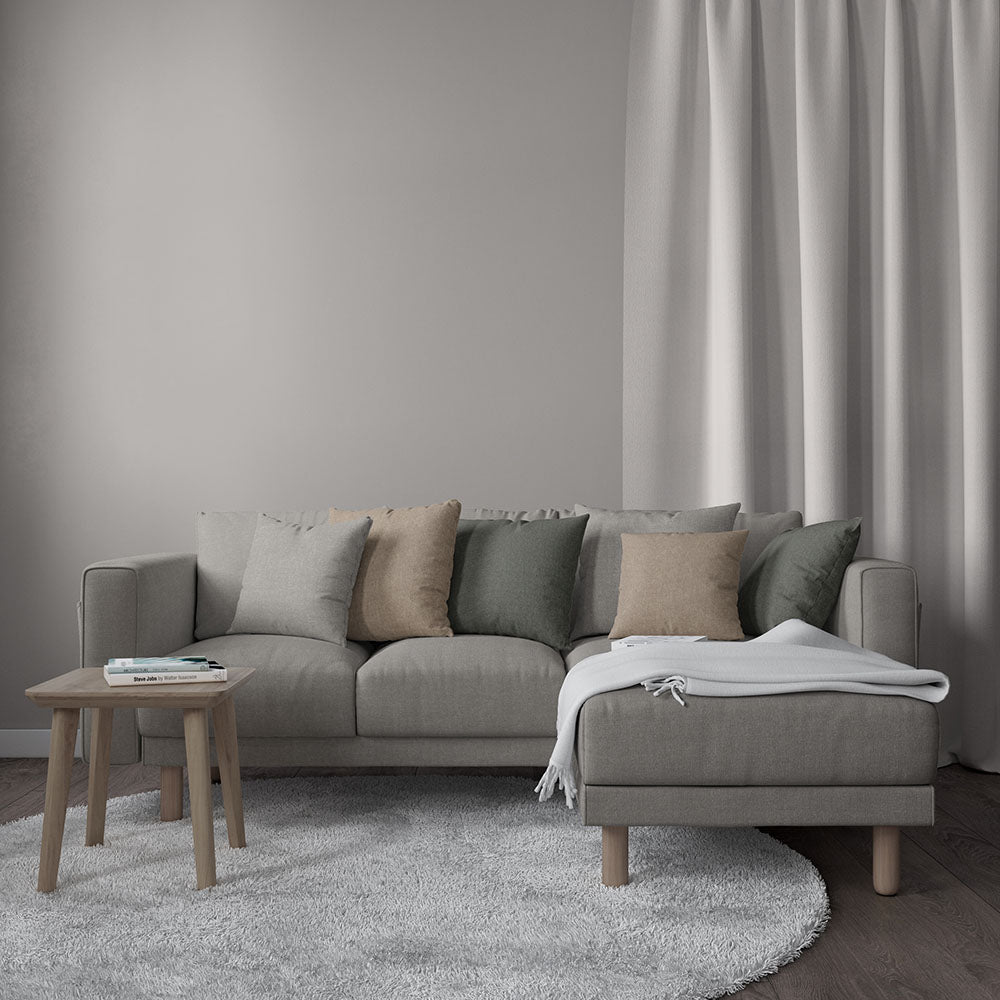 Light gray modular sofa with chaise, beige and sage cushions, wooden legs, soft rug, side table, and throw blanket.
