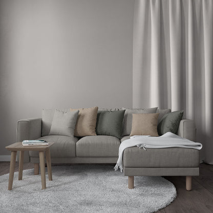 Light gray modular sofa with chaise, beige and sage cushions, wooden legs, soft rug, side table, and throw blanket.