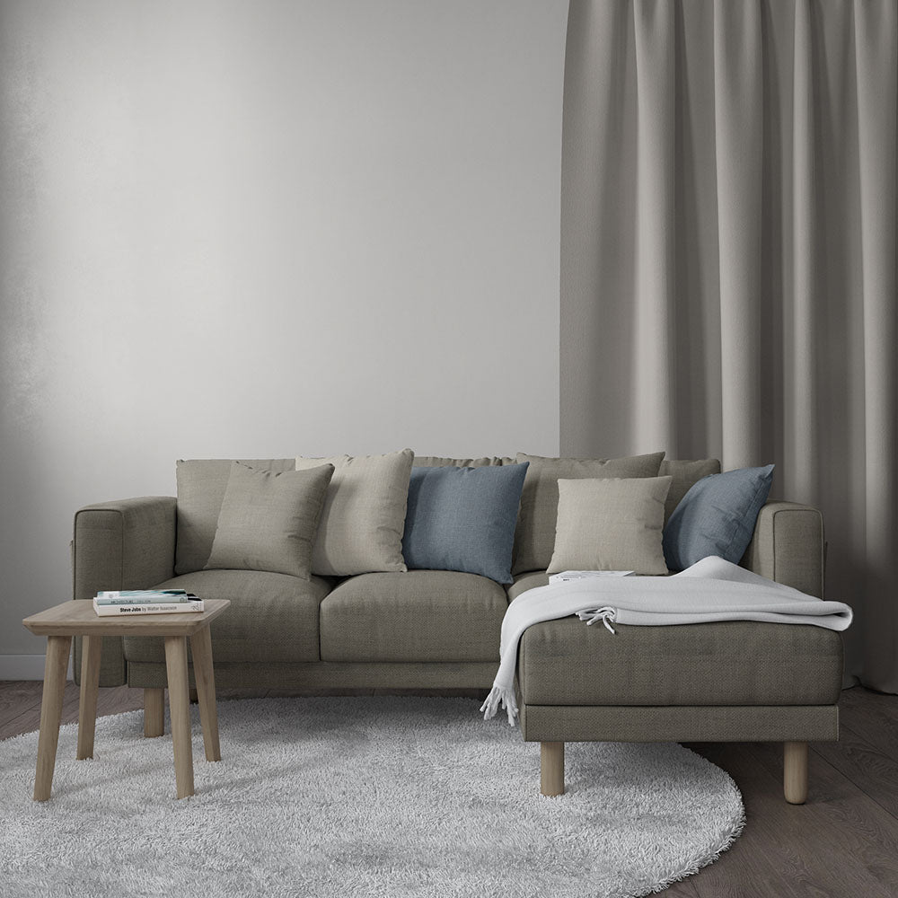 Taupe sectional sofa with chaise, beige and blue cushions, light wood legs, white throw, small wooden side table, gray rug.