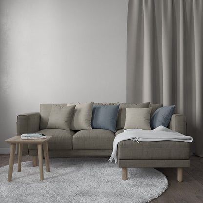 Taupe sectional sofa with chaise, beige and blue cushions, light wood legs, white throw, small wooden side table, gray rug.