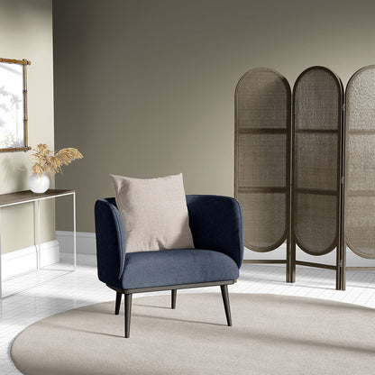 Dark blue velvet armchair with beige cushion, mid-century legs, in a neutral living room with a woven screen divider.