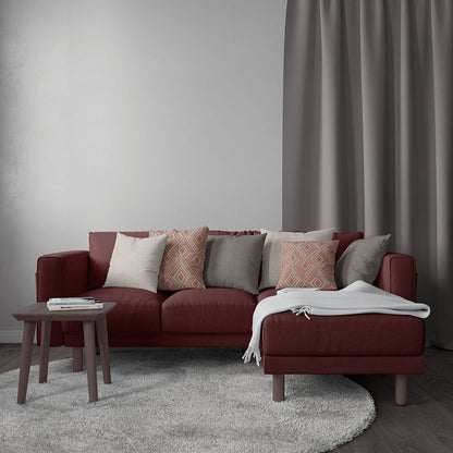 Maroon fabric sectional with chaise, mixed cushions, grey throw, round light-grey rug, small wood side table, grey curtains.