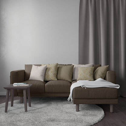 Brown sectional sofa with beige and patterned cushions, chaise with white throw, wooden side table, grey rug and curtains.