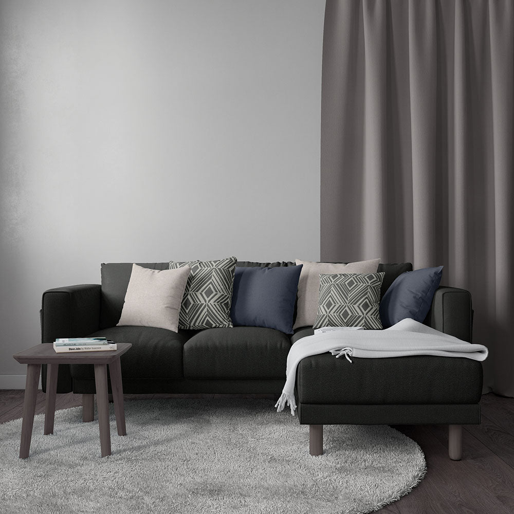 Dark gray sectional sofa with mixed geometric pillows, light throw, small round coffee table, gray rug & curtains.