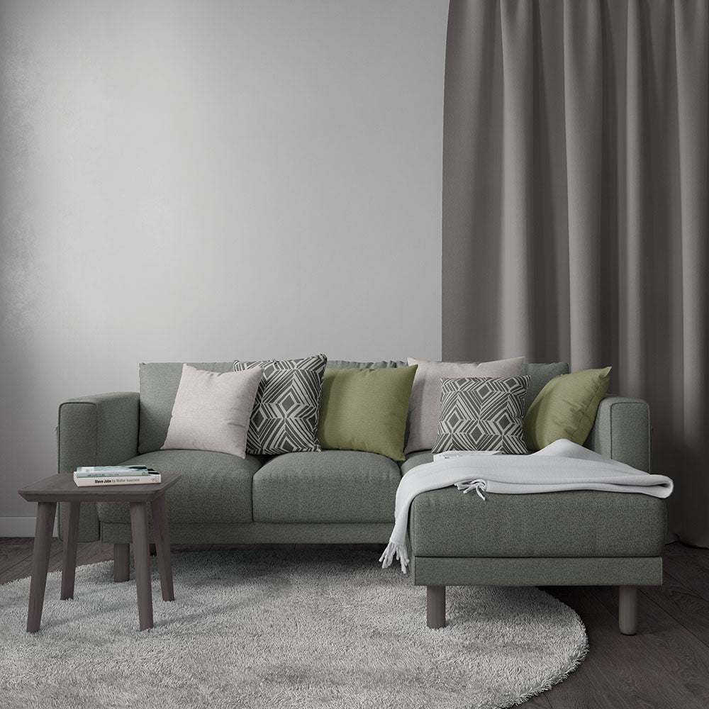 Olive-green fabric sectional with chaise, tapered wooden legs, mixed pink-green-gray cushions; gray rug and throw blanket.