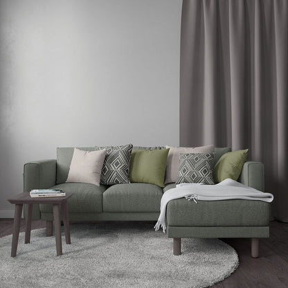 Olive-green fabric sectional with chaise, tapered wooden legs, mixed pink-green-gray cushions; gray rug and throw blanket.