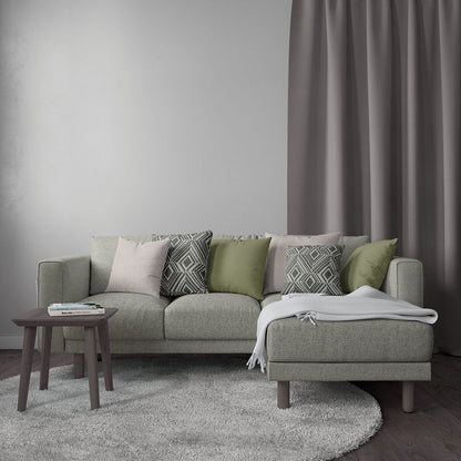 Light gray modular sofa with green and gray cushions, pink accent, gray throw, round dark wood side table, taupe drapes.