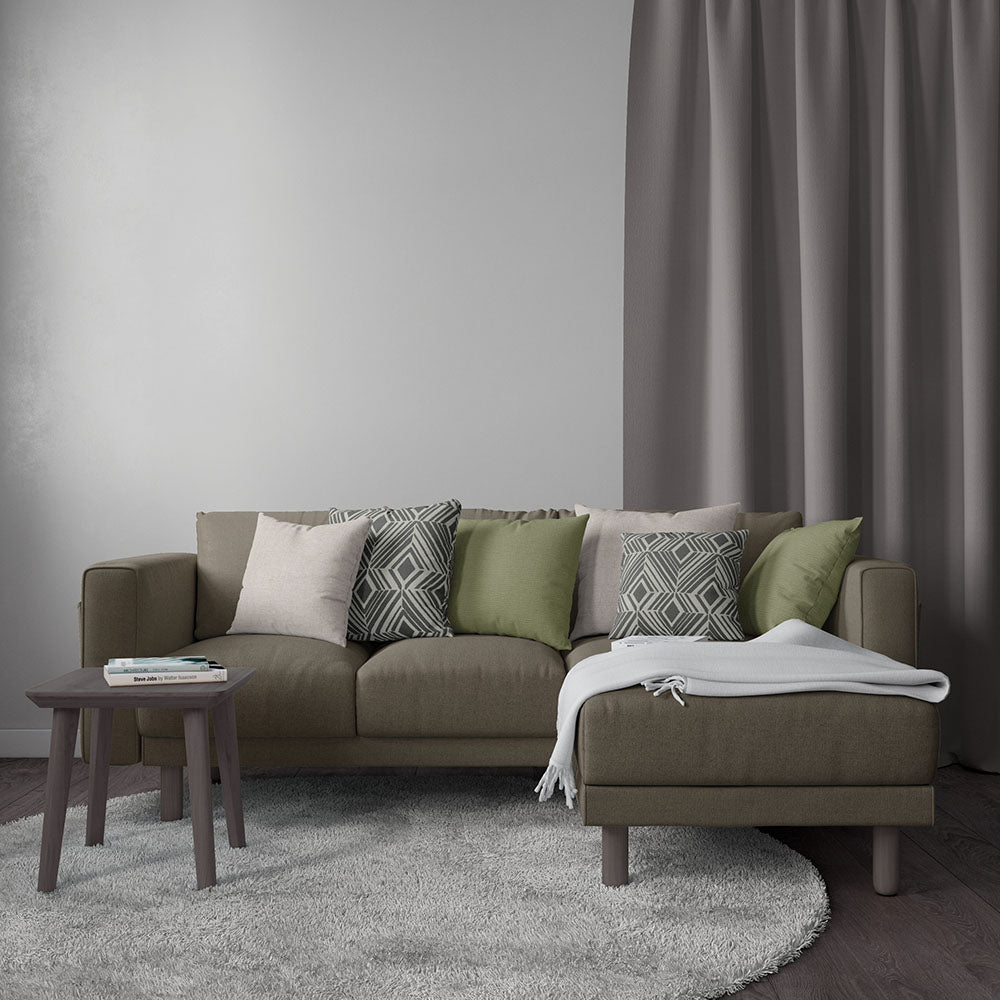 Olive-brown sectional with chaise, mix of cream, sage and geometric cushions; white throw, gray rug, and small dark wood side table.