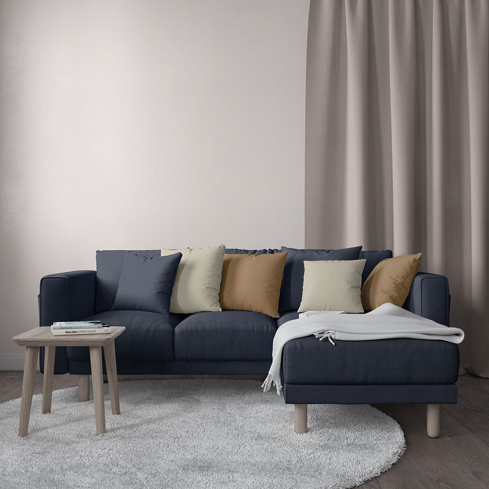 Dark navy L-shaped sectional sofa with tan, cream, and olive cushions; light gray throw on chaise, round wood legs.
