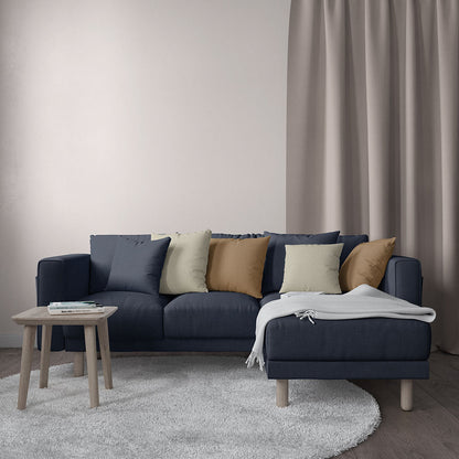 Dark navy L-shaped sectional sofa with tan, cream, and olive cushions; light gray throw on chaise, round wood legs.
