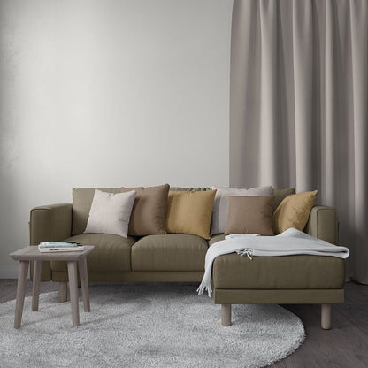 Olive-tan fabric sectional with chaise, neutral throw pillows, light wood legs, round side table, gray rug and curtains.