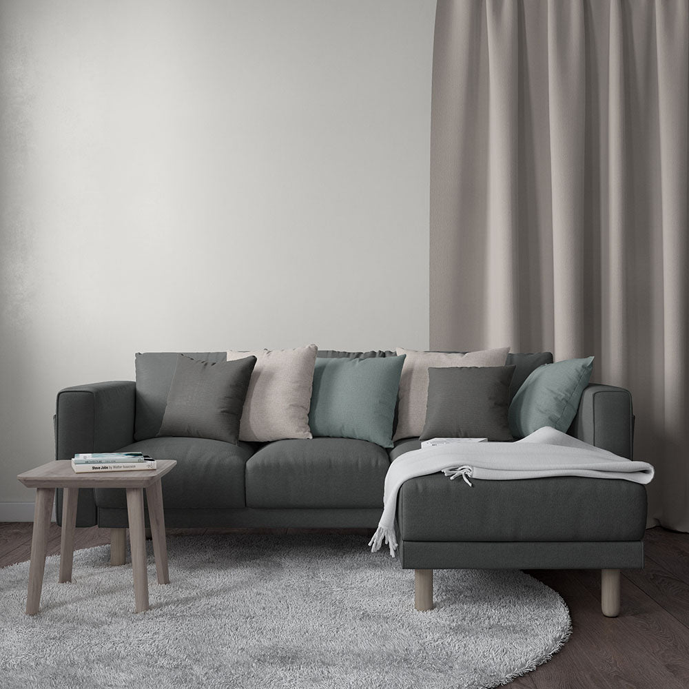 Dark gray sectional with beige, gray, teal cushions, white throw, wooden legs, chaise on the right; round light rug.
