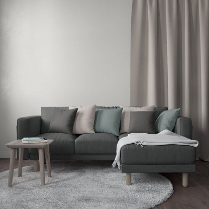 Dark gray sectional with beige, gray, teal cushions, white throw, wooden legs, chaise on the right; round light rug.